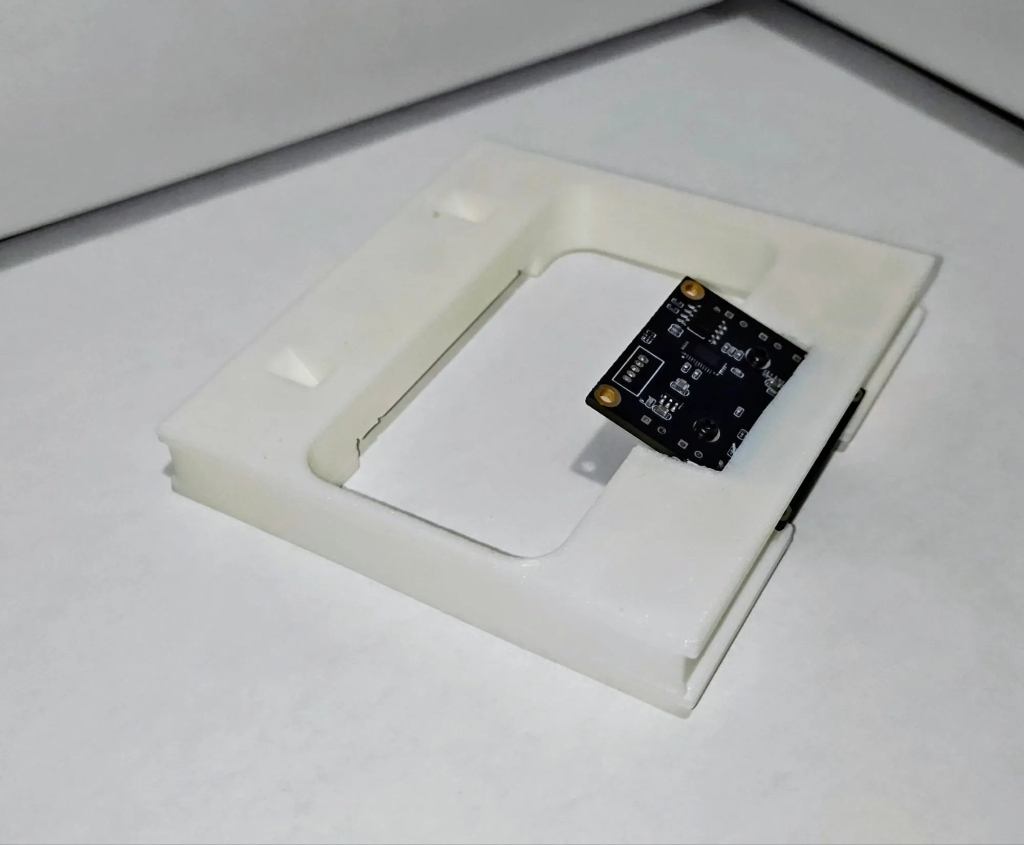 Small camera circuit board seated in a white 3D printed mounting plate