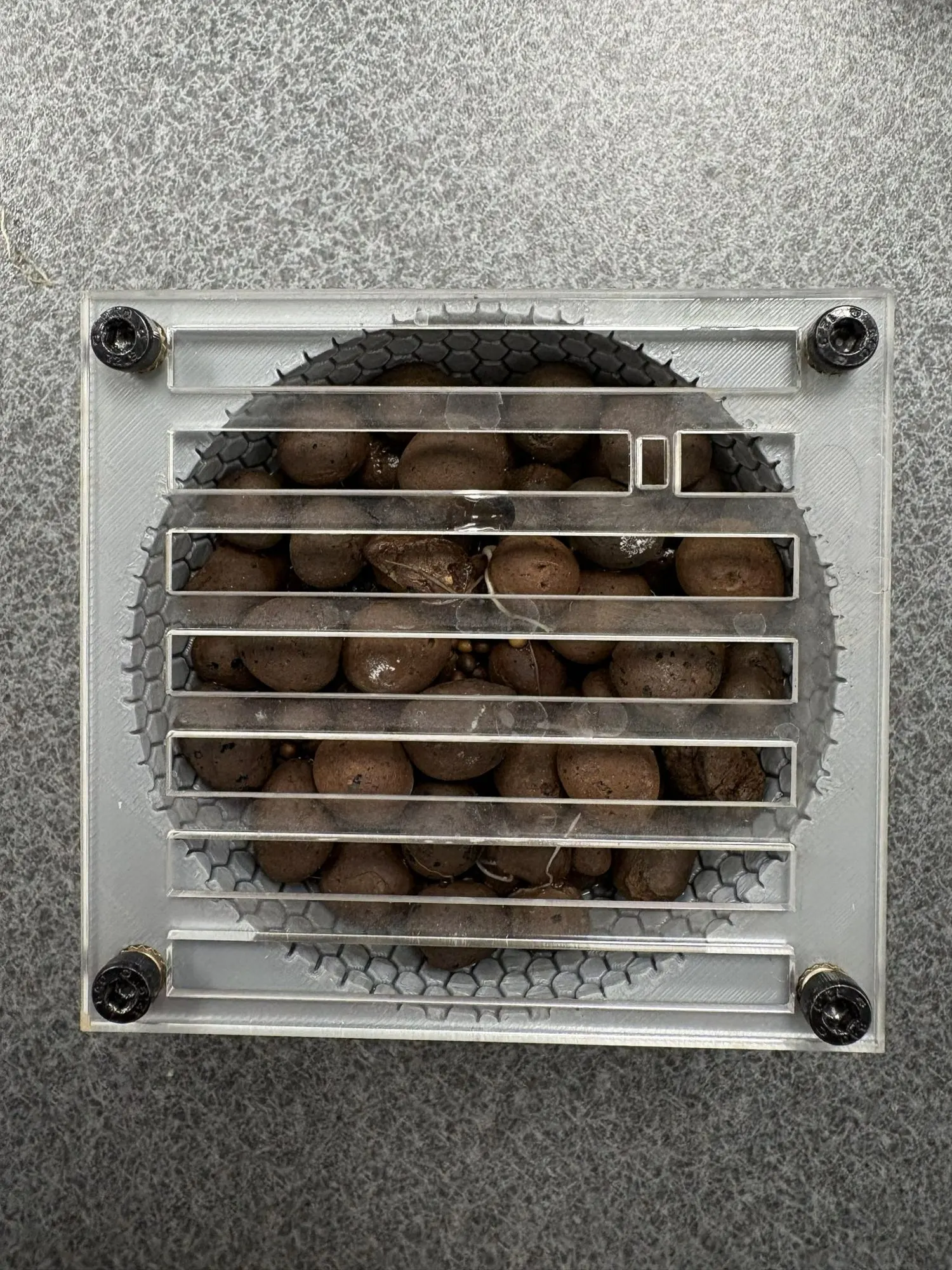 Clear slotted grate holding brown clay pebbles over the hex dome