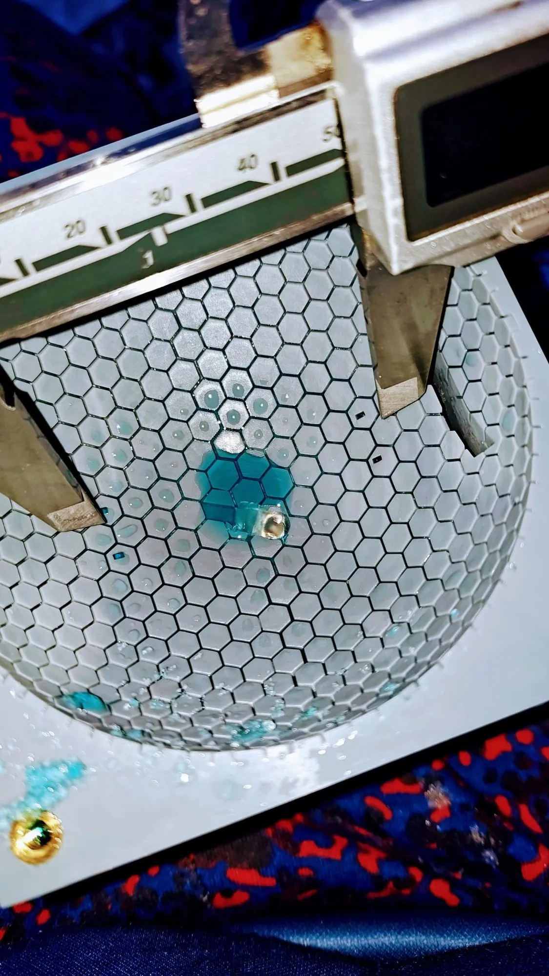 Digital caliper jaws spanning a grooved dome with blue dyed water spreading through the hex channels