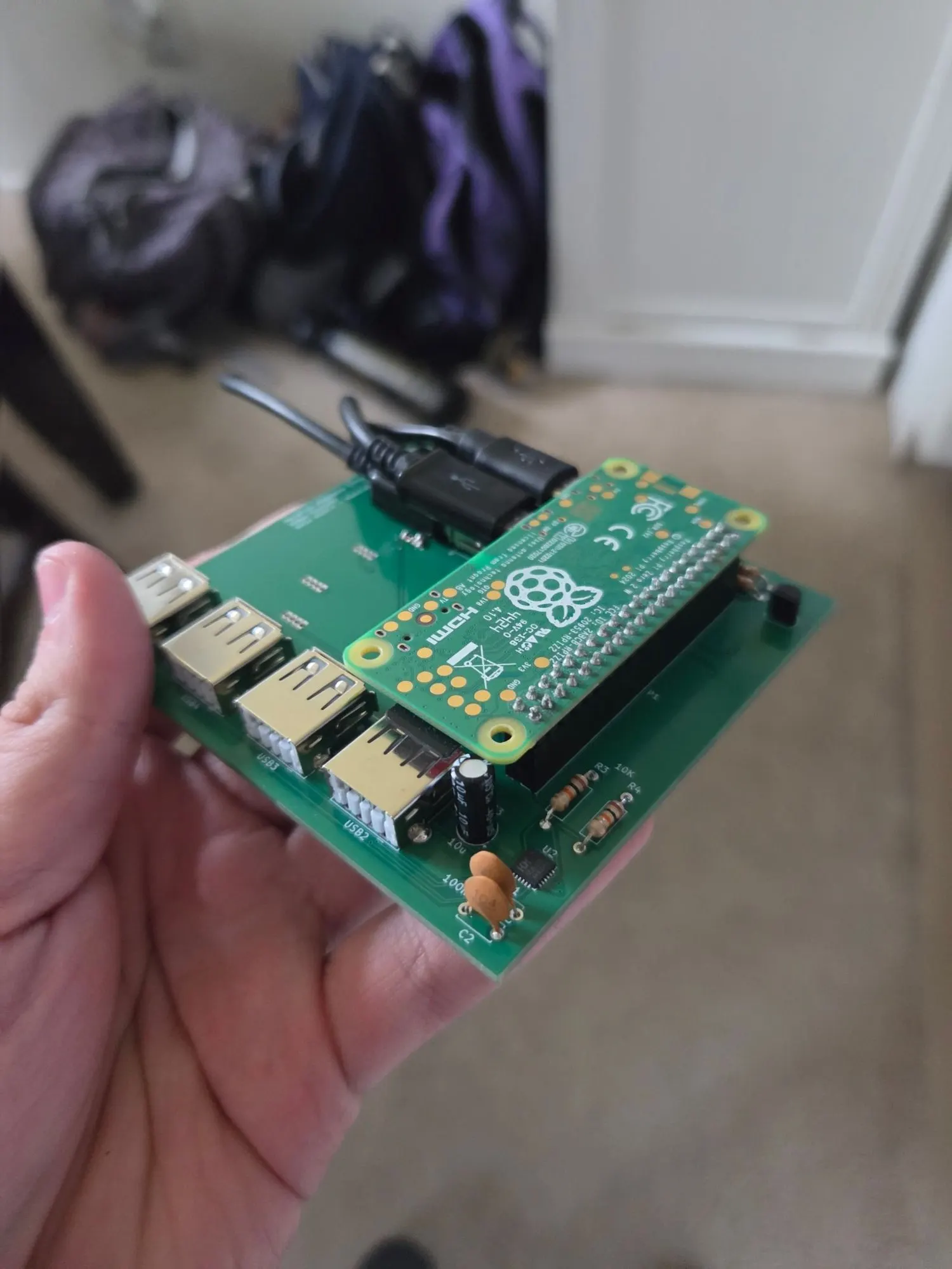 A hand holding a Raspberry Pi mounted on a green carrier board with headers and USB ports