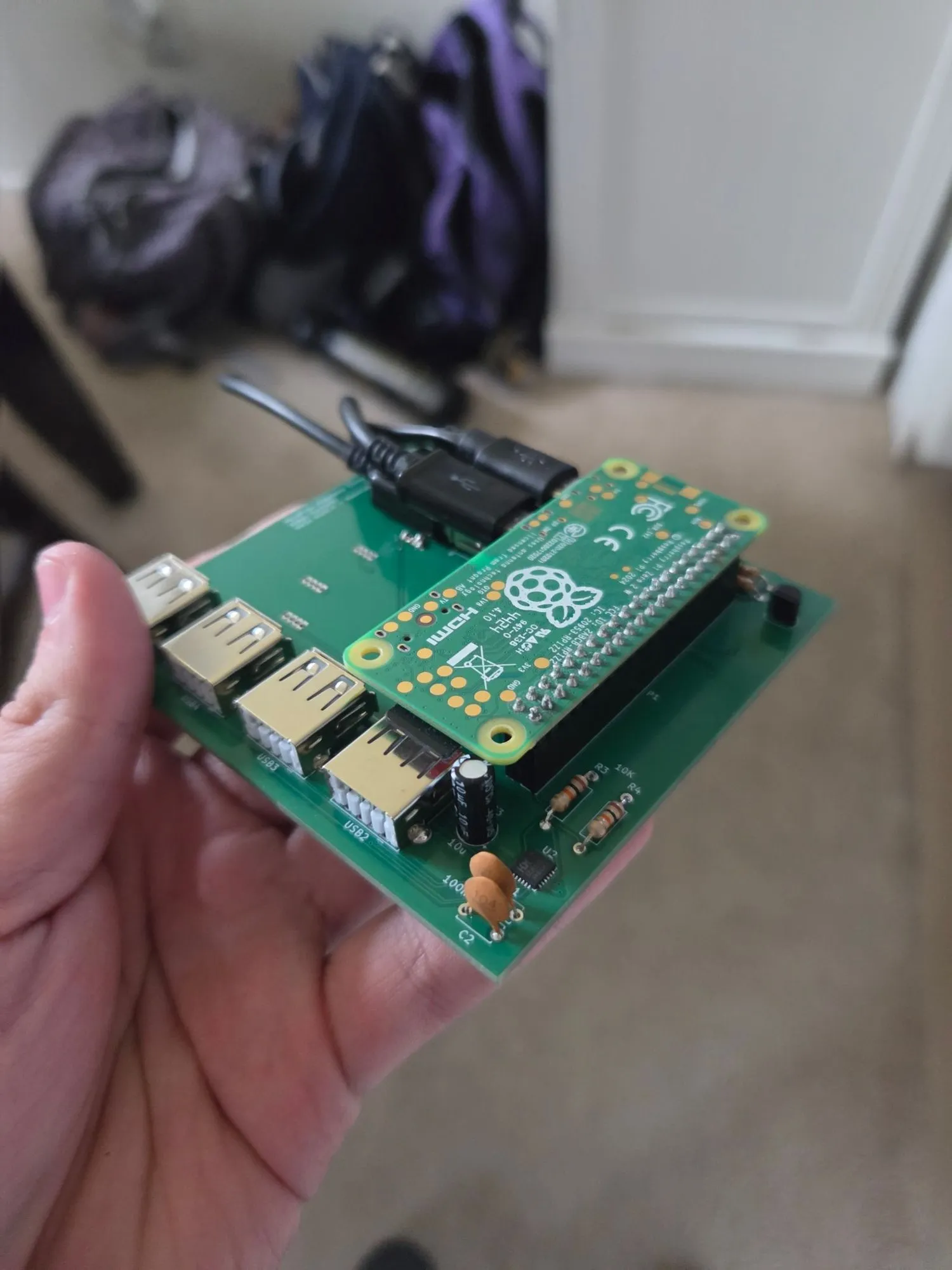 Hand holding a green custom circuit board with four USB ports and a Raspberry Pi Zero 2 W mounted on top