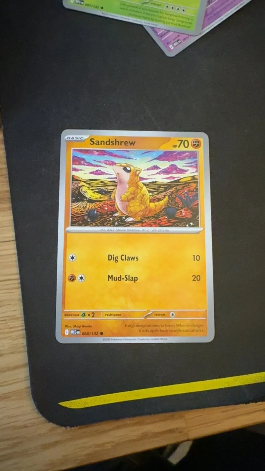 A real scan: a Sandshrew card lying flat on a black desk mat with a yellow stripe along the edge.